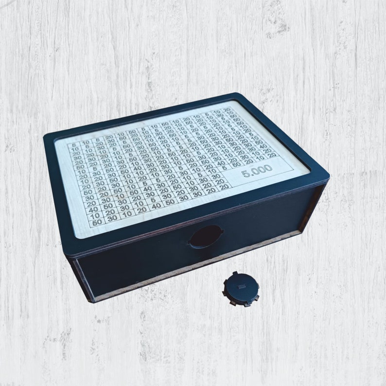 May include: A black wooden box with a grid of numbers and the text "5.000" printed on the front. The box has a small round hole on the top.