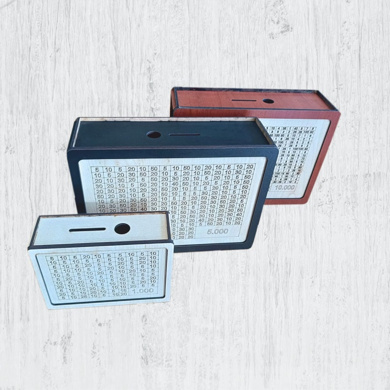 May include: Three wooden money boxes with a grid pattern and numbers. The boxes are black, brown, and white. The boxes have a slot on the top for inserting money. The boxes have a total amount printed on the front. The black box has a total of $6,000, the brown box has a total of $10,000, and the white box has a total of $1,000.