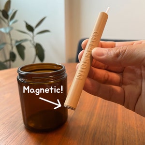 May include: A brown wooden wick dipper with the text "WICKSTIGO" printed on it. The dipper is magnetic and is being held near a brown glass jar with the word "Magnetic!" written on it.