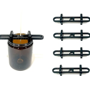 May include: A black candle centering tool is placed on a brown glass jar with a white wick. Four additional black centering tools are displayed on a white background. The tools are designed to keep candle wicks centered during the candle-making process.