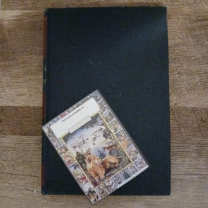 May include: A dark-covered hardcover book with a decorative sticker. The sticker has a colourful illustration of lions and other animals, with the text "This book property of" at the top.