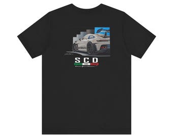 May include: Black t-shirt featuring a graphic of a white sports car with a spoiler. The image includes the text "SCD" above a green, white, and red bar, and the words "Drive Your Dreams".