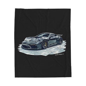 May include: A black blanket featuring a detailed illustration of a black sports car with yellow brake calipers. The car is depicted on a textured, light gray surface, set against a black background. The blanket has a soft, plush appearance.