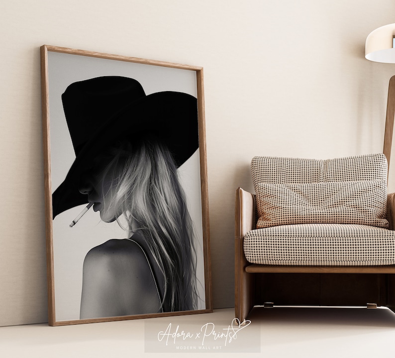 May include: Black and white photograph of a woman wearing a wide-brimmed hat and looking away from the camera. She is holding a cigarette in her mouth.