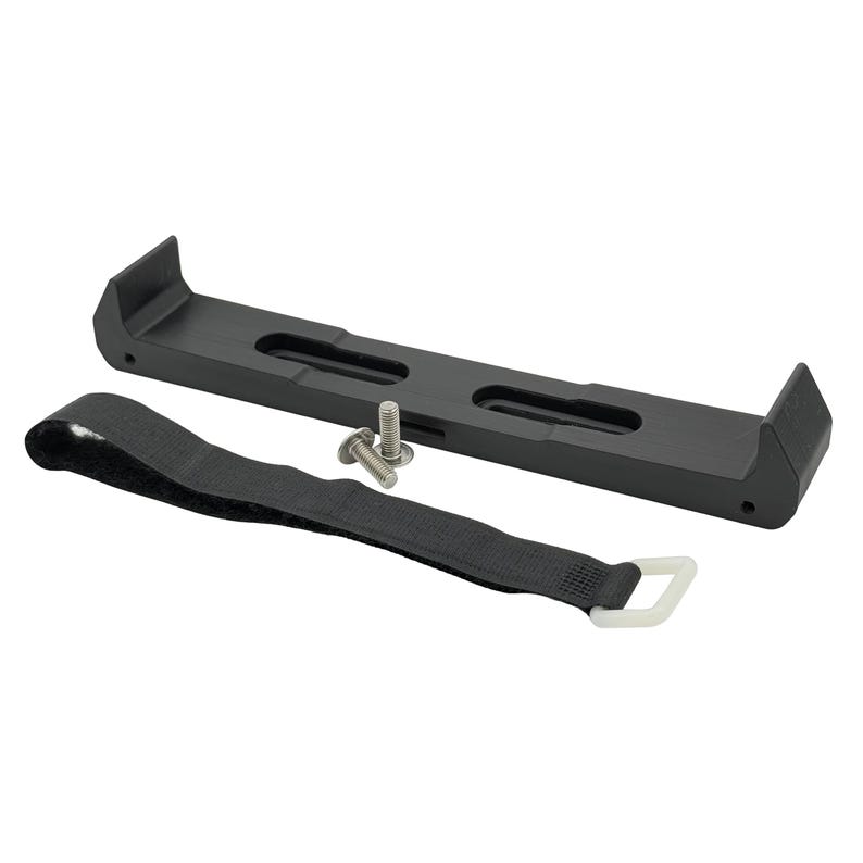 May include: A black metal bracket with two slots and raised ends, alongside a black strap with a white plastic loop and two silver screws. The bracket is designed to hold an item.