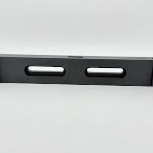 May include: A black plastic shelf bracket with two rectangular cutouts. The bracket is designed to support a shelf.