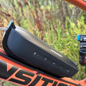 May include: A black Bose SoundLink Flex Bluetooth speaker attached to a red mountain bike frame. The speaker has volume controls and a power button.