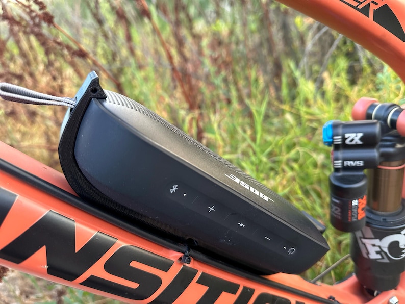 May include: A black Bose SoundLink Flex Bluetooth speaker attached to a red mountain bike frame. The speaker has volume controls and a power button.