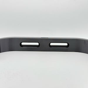 May include: A black plastic 3D printed phone stand with two slots for holding a phone.