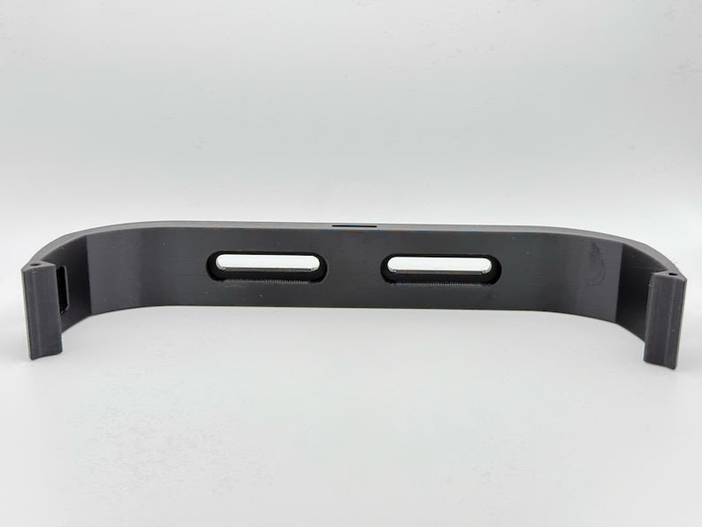 May include: A black plastic 3D printed phone stand with two slots for holding a phone.