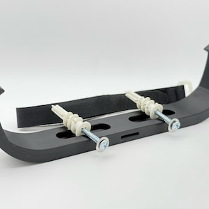 May include: Black plastic wall mount bracket with two white plastic anchors and screws. The bracket has a curved shape and is designed to hold a pipe or cable.