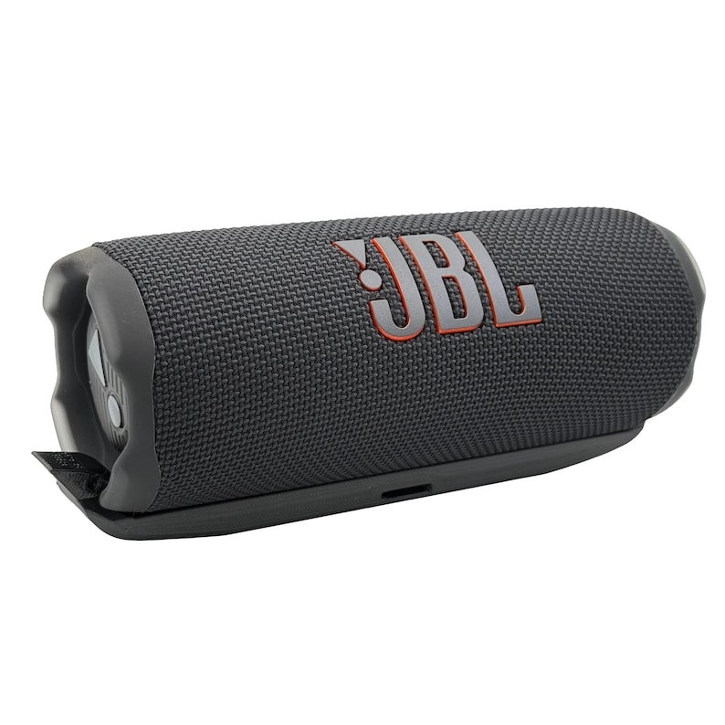 May include: A dark gray JBL portable Bluetooth speaker with the JBL logo in orange. The speaker has a cylindrical shape with rounded ends and a textured fabric exterior. It features a built-in control panel and a black base.