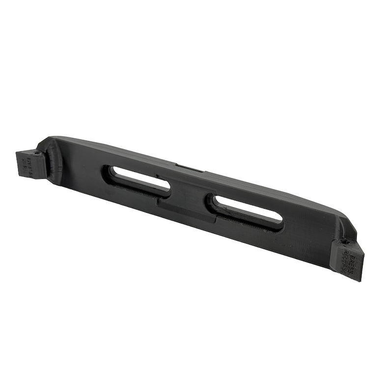 May include: A black, elongated metal object with two rectangular cutouts and angled ends. The object appears to be a component or part of a larger mechanism, possibly for industrial or mechanical use. The ends have text.