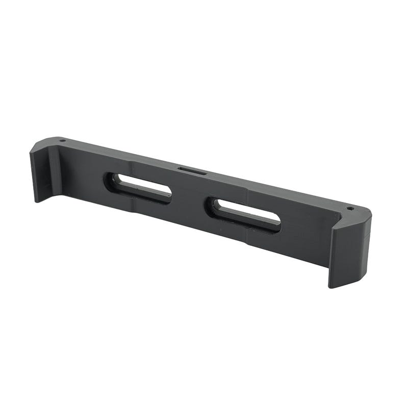 May include: A black, rectangular bracket with two elongated oval cutouts and a small hole. The bracket has two raised, right-angled end pieces. The object is made of a matte material and is set against a white background.