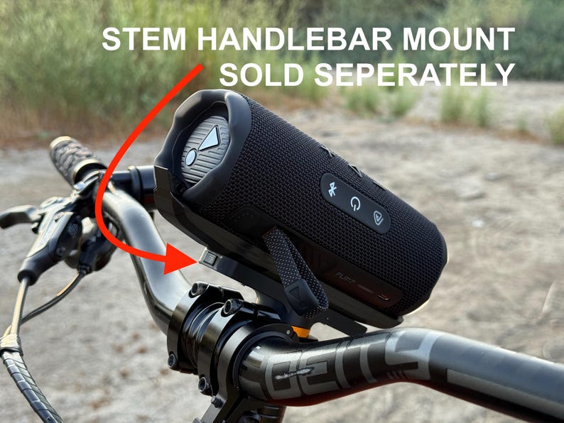 May include: A black portable speaker mounted on a bicycle handlebar. The speaker is cylindrical with control buttons and a mesh cover. The text "STEM HANDLEBAR MOUNT SOLD SEPERATELY" is visible above the speaker.