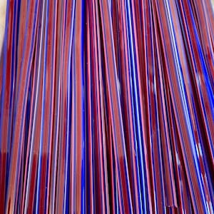 May include: A bundle of thin glass rods with alternating red and blue stripes. The rods are arranged in a vertical pattern, creating a colorful and textured background.