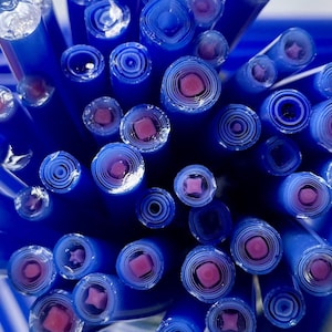 May include: Close-up of a bundle of blue glass rods with pink and white swirls inside. The rods are arranged in a circular pattern, showing the cross-section of each rod.