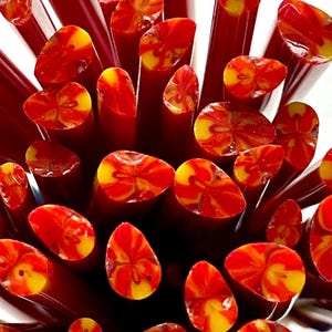 May include: A close-up of a bundle of red and yellow glass rods. The rods have a swirling pattern of red and yellow.