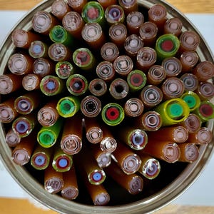 May include: A tin can filled with colorful glass rods, each with a different pattern of concentric circles. The rods are arranged in a circular pattern, with the ends of the rods facing the viewer.
