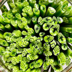 May include: A close-up view of a bunch of green glass rods with black leaf designs. The rods are arranged in a circular pattern, creating a visually appealing display.