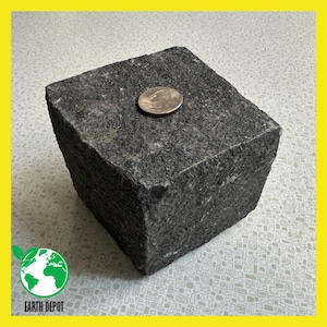 May include: A dark gray, cube-shaped granite stone with a quarter coin on top. The stone has a rough, textured surface. The Earth Depot logo is in the lower left corner.