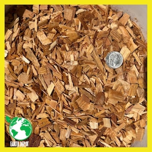 May include: A collection of light to medium brown wood chips of varying sizes and shapes. A silver United States quarter coin is placed among the wood chips to provide a visual scale reference for the size of the individual pieces of wood.