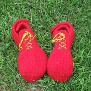 Pode incluir: Um par de pantufas vermelhas de malha com cadarços amarelos. As pantufas estão sobre um leito de grama verde.
