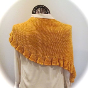 May include: A mustard yellow knitted shawl with a scalloped edge. The shawl is draped over a white shirt on a mannequin.