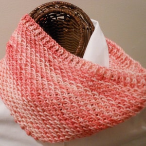 May include: A pink and white knitted infinity scarf with a textured pattern.