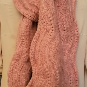May include: A pink knitted scarf with a wavy cable knit pattern.