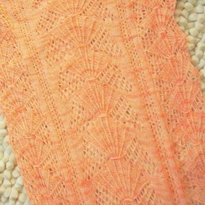 May include: A close-up of a peach-colored crocheted fabric with a delicate, lacy pattern.