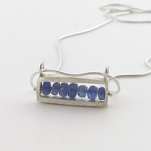 May include: A silver necklace with a rectangular pendant containing a row of blue sapphire stones.