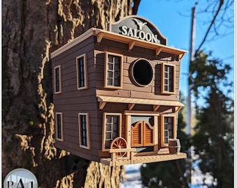 May include: A wooden birdhouse shaped like a Western saloon with a sign that reads "SALOON". The birdhouse has a brown wooden exterior with tan accents and a barrel on the porch.