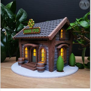 May include: A detailed miniature Irish pub model with a gray tiled roof, wooden beams, and stone walls. The sign reads "Irish Pub" with a green shamrock. The windows glow with warm light, and two barrels sit in front.