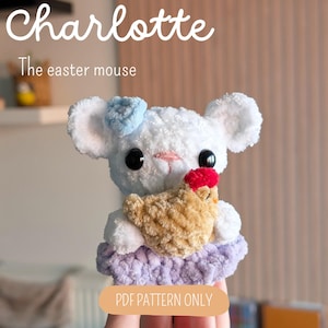 Peut inclure: Une peluche souris crochetée blanche avec un nœud bleu clair, tenant un petit poulet beige avec une crête rouge. La souris porte une jupe violet clair. Le texte indique : Charlotte The easter mouse et PDF PATTERN ONLY.
