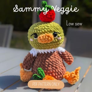 Peut inclure: Un jouet en peluche crocheté avec une tête verte surmontée d'une fraise rouge, un corps marron et des pieds orange. Le texte Sammy Veggie, Low sew et PDF PATTERN ONLY est visible. Le jouet a des yeux noirs, des joues roses et un col blanc.