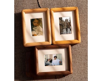 May include: Three wooden picture frames with different colored wood tones. The frames are arranged in a staggered formation. The top two frames are light brown and the bottom frame is a darker brown. Each frame has a white mat and a photo inside.