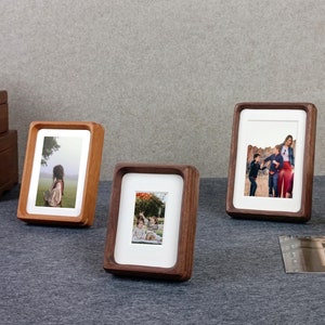 Könnte beinhalten: Vier Holzbilderrahmen mit Fotos in verschiedenen Größen. Die Rahmen sind alle braun und haben ein schlichtes Design. Die Fotos zeigen verschiedene Motive, darunter eine Frau auf einem Feld, eine Familie, die in einem Park spazieren geht, und eine Gruppe von Menschen, die zusammen stehen.