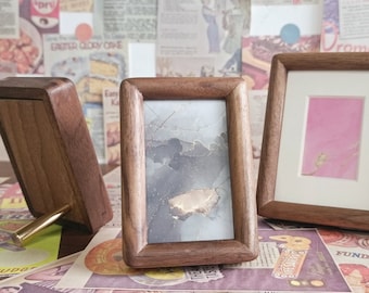 May include: Three wooden picture frames with different sized openings. The frames are all brown and have a rustic look. The frames are sitting on a table with a variety of patterned paper underneath.