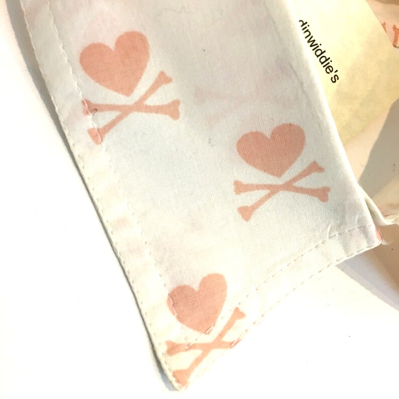 May include: A white fabric collar with a pink heart and crossbones pattern. The text "dinwiddie's" is visible on the collar.