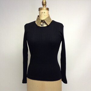 May include: Black long-sleeve ribbed shirt with a round neckline. The shirt is on a mannequin wearing a beige collar.