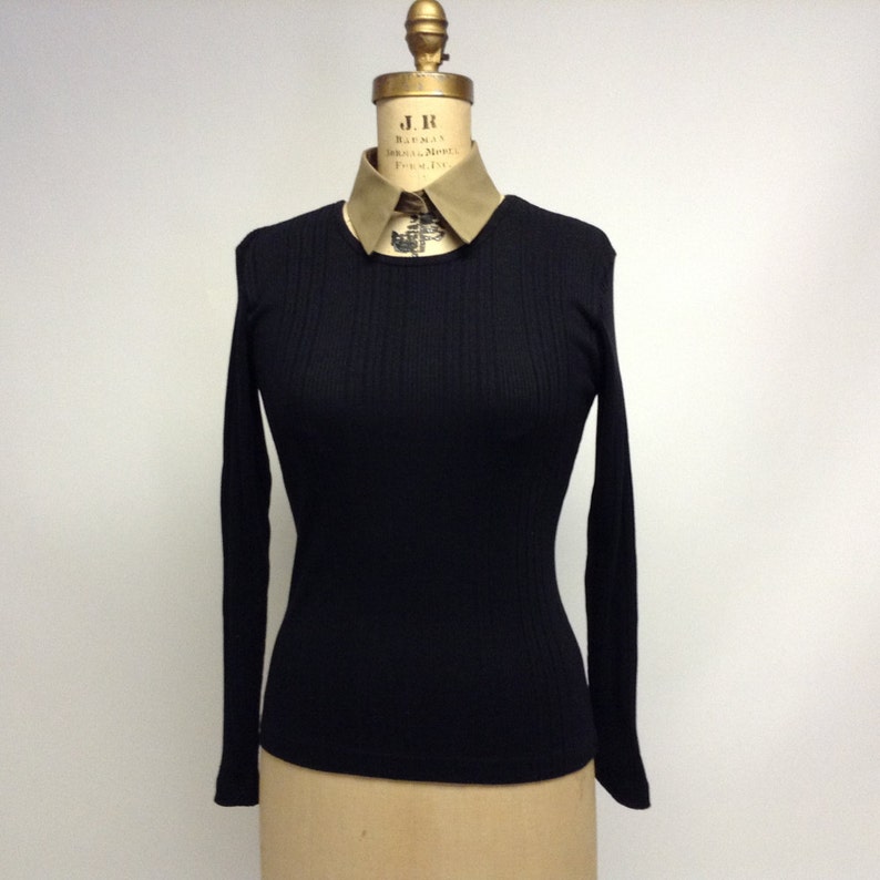 May include: Black long-sleeve ribbed shirt with a round neckline. The shirt is on a mannequin wearing a beige collar.