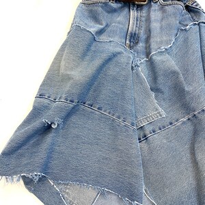 May include: A blue denim skirt with a brown leather belt. The skirt is made from multiple layers of denim and has a frayed hem.