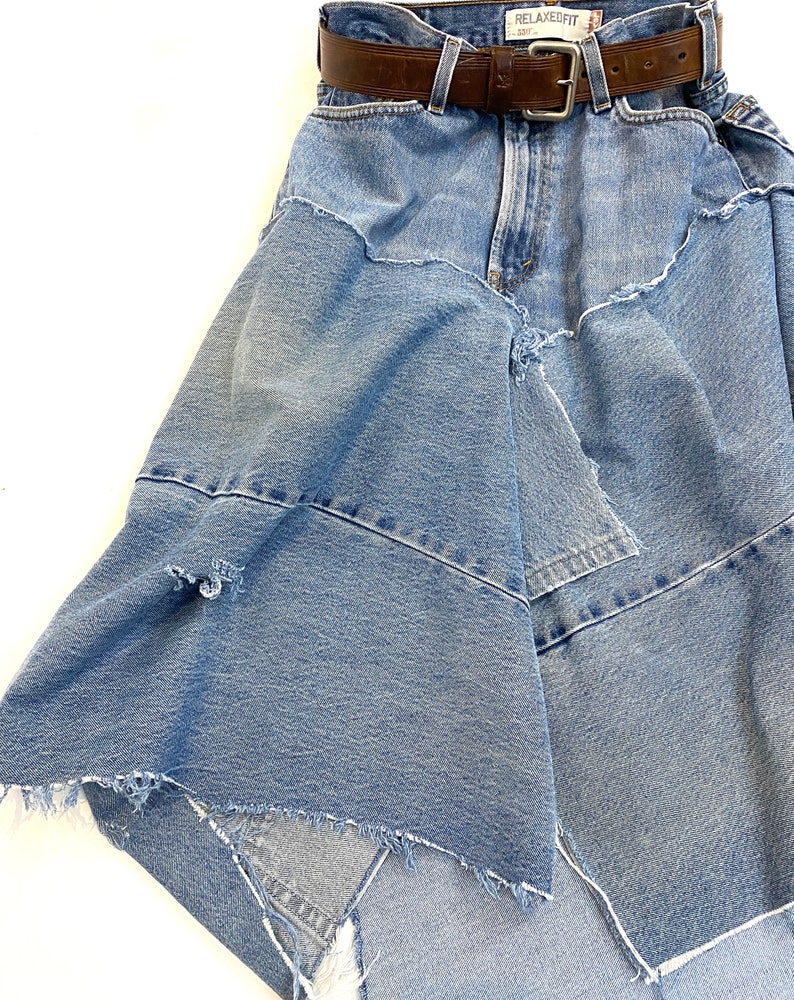 May include: A blue denim skirt with a brown leather belt. The skirt is made from multiple layers of denim and has a frayed hem.
