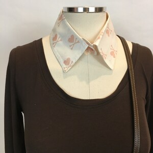 May include: A brown long-sleeved shirt with a white detachable collar featuring a pink heart and crossbones pattern.