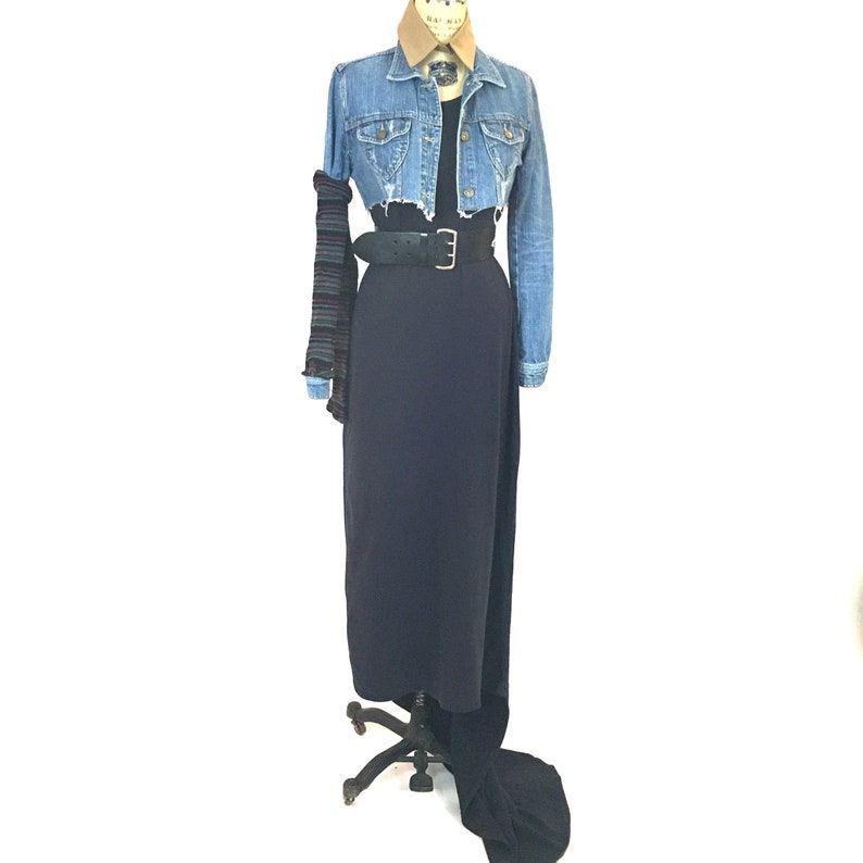 May include: A long, dark blue maxi skirt with a denim jacket and a black belt. The jacket is cropped and has a brown collar.
