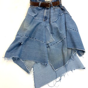 May include: A blue denim skirt with a brown leather belt. The skirt is made of multiple layers of denim and has a frayed hem.