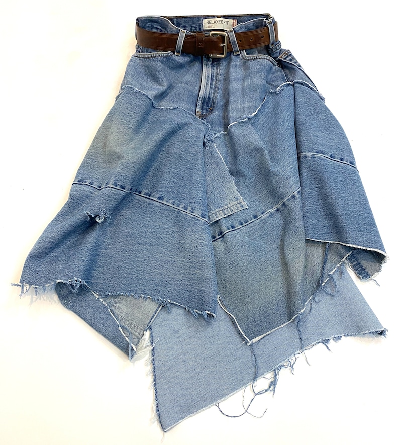 May include: A blue denim skirt with a brown leather belt. The skirt is made of multiple layers of denim and has a frayed hem.