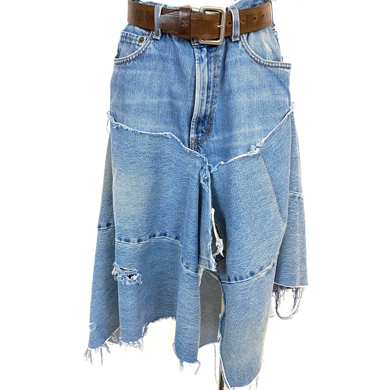 May include: A blue denim skirt with a brown leather belt. The skirt is distressed and has a frayed hem.