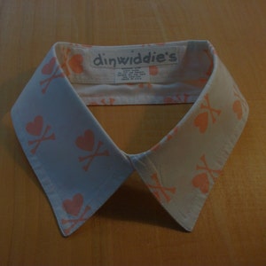 May include: A white cotton collar with a pink and white skull and heart pattern. The collar has a label that reads "dinwiddie's".